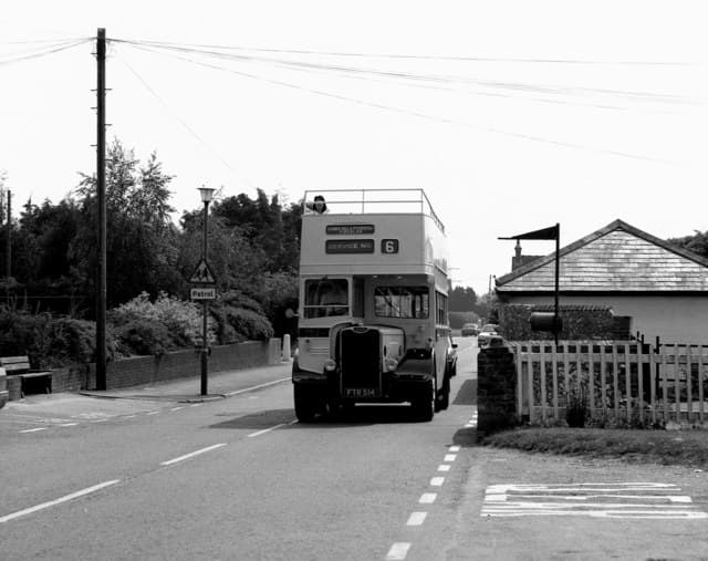 An open-top vintage bus passing through Clanfield village